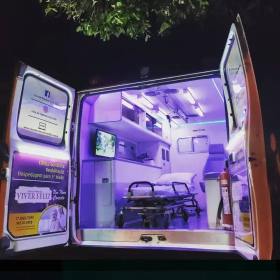 Interior da ambulância iluminado em lilás, com maca, armários e monitor