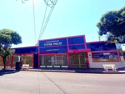 Fachada magenta e azul-escura com o letreiro "Casa de Repouso Viver Feliz — um novo conceito", árvores na calçada