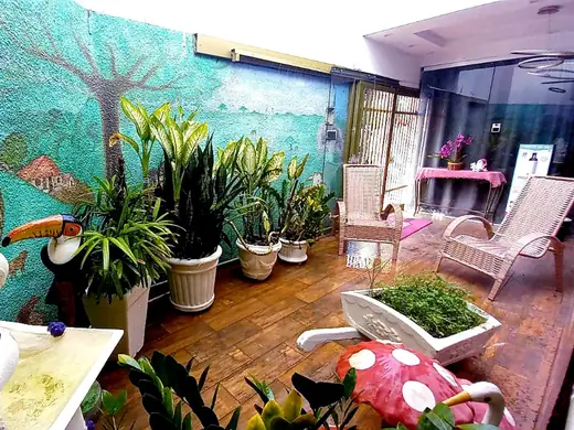 Jardim com parede pintada de árvore e tucano, vasos de plantas e cadeiras de balanço brancas