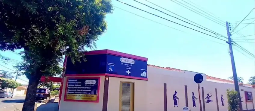 Esquina da casa: bloco com o letreiro Viver Feliz e muro branco com silhuetas pintadas de idosos caminhando e dançando (quadro do vídeo)