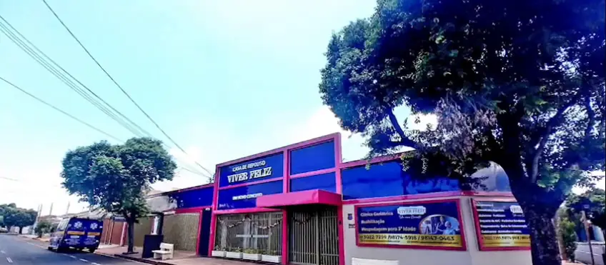 Fachada vista da rua, com o letreiro Viver Feliz, as faixas da clínica e a ambulância estacionada à esquerda (quadro do vídeo)