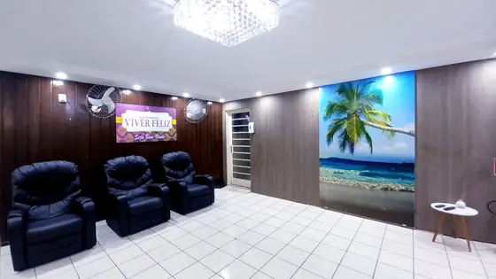 Sala com três poltronas reclináveis pretas, painel de praia e o letreiro Viver Feliz