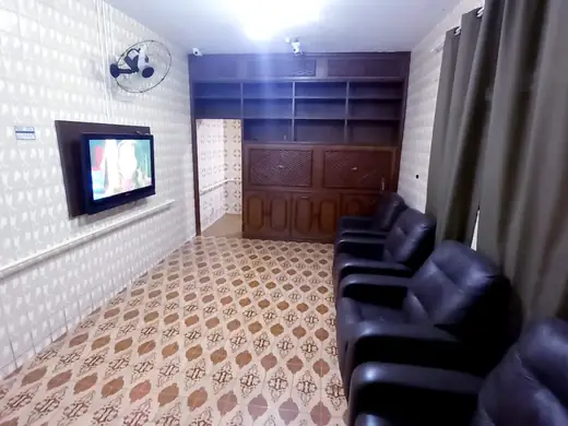 Sala de piso estampado com poltronas pretas, TV e estante de madeira